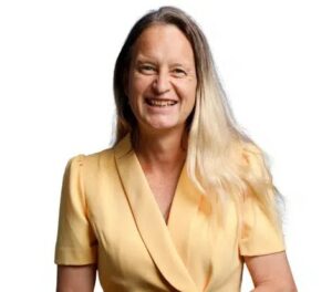Woman wearing a yellow jacket, has long blonde hair and is smiling at the camera