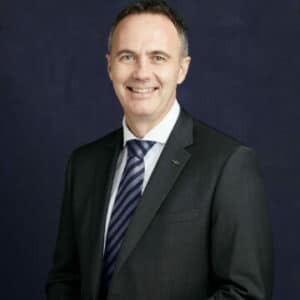 Person wearing black suit with a navy background