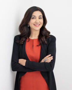 Lisa Annese in a red dress and black jacket, in front of a grey background.