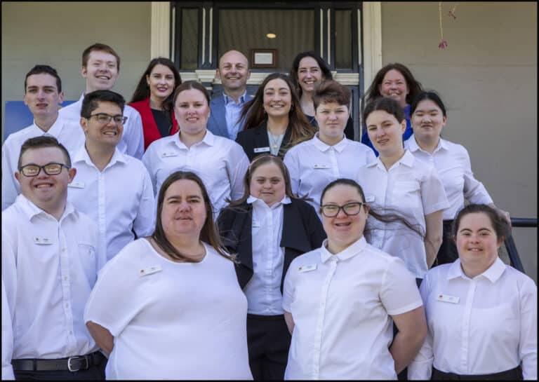 The staff at Hotel Etico pose together outside a building in white uniforms, smiling at the camera.