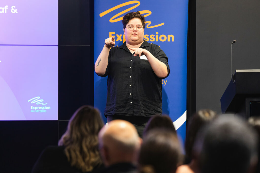 Sherrie Beaver standing in front of an audience using sign language 