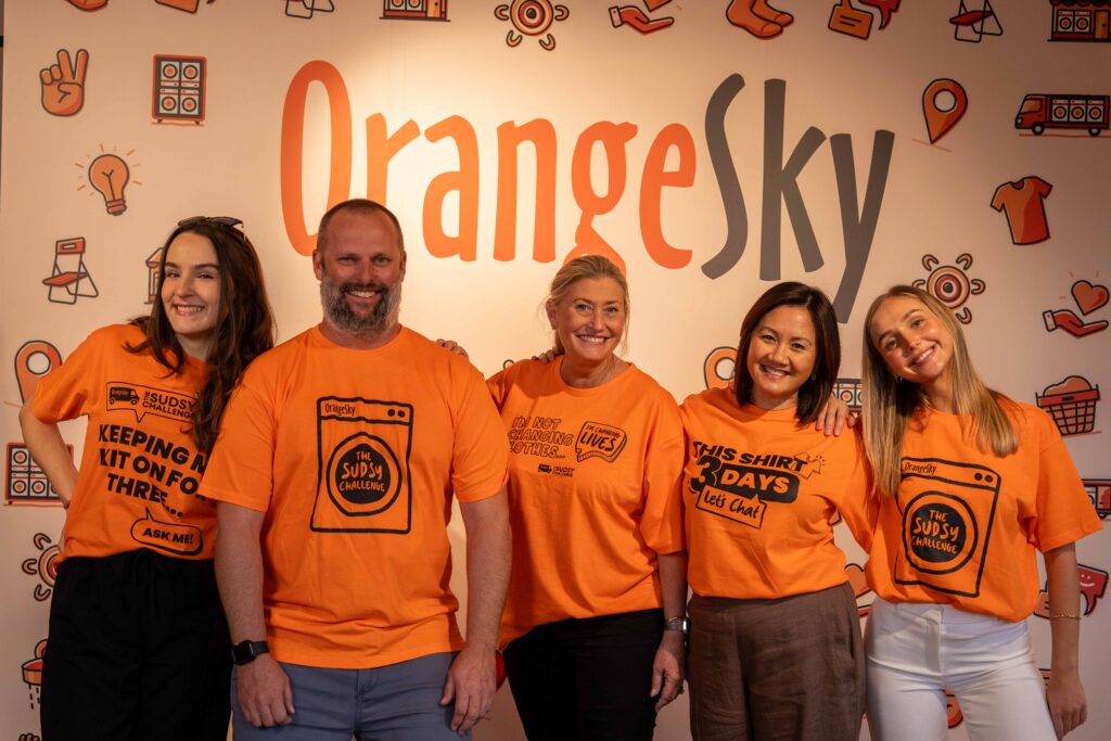 A group of people wearing orange t-shirts stand in front of a banner that says Orange Sky.