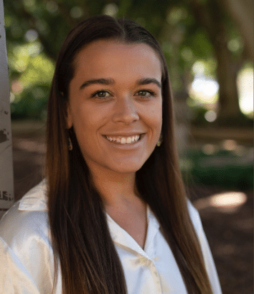 Abbey Wright wearing a white shirt, has long brown hair and is smiling at the camera.