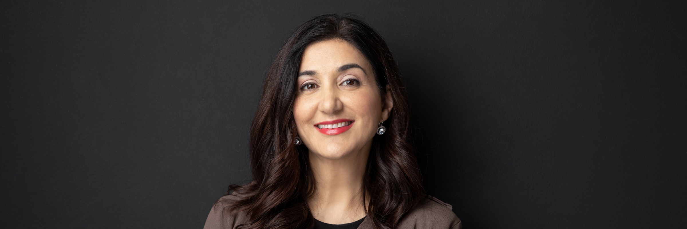 Lisa Annese in a brown and grey suit, in front of a dark grey background.